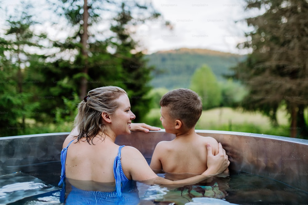 A mother with her little son enjoying bathing in wooden barrel hot tub in the mountains.