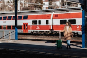 A young traveler woman with luggage waiting for train at train station platform. Train in the background.