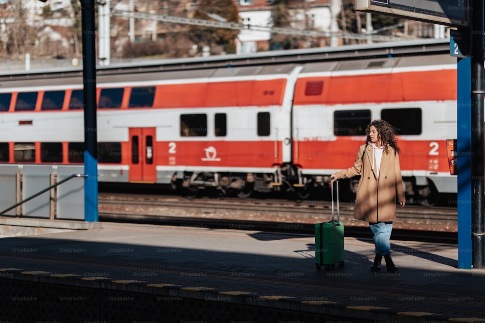A young traveler woman with luggage waiting for train at train station platform. Train in the background.