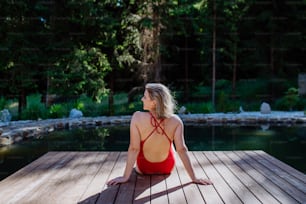 Uma visão traseira da mulher jovem em traje de banho sentada no cais do lago durante as férias de verão nas montanhas.
