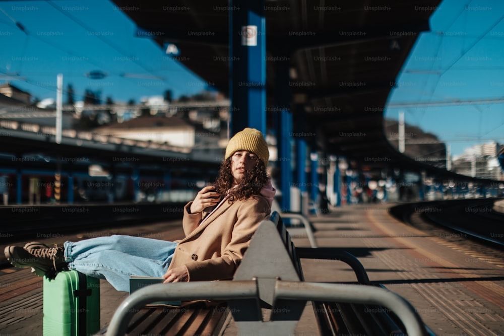 駅のホームに荷物を持って一人で座っている若い旅行者の女性。