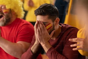 Worried football fans supproting a spanish national team in live soccer match at stadium.