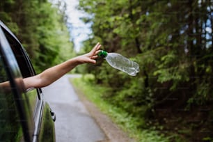 Una mano di donna che getta via la bottiglia di plastica dal finestrino dell'auto sulla strada nella natura verde, protezione dell'ambiente, concetto di riscaldamento globale