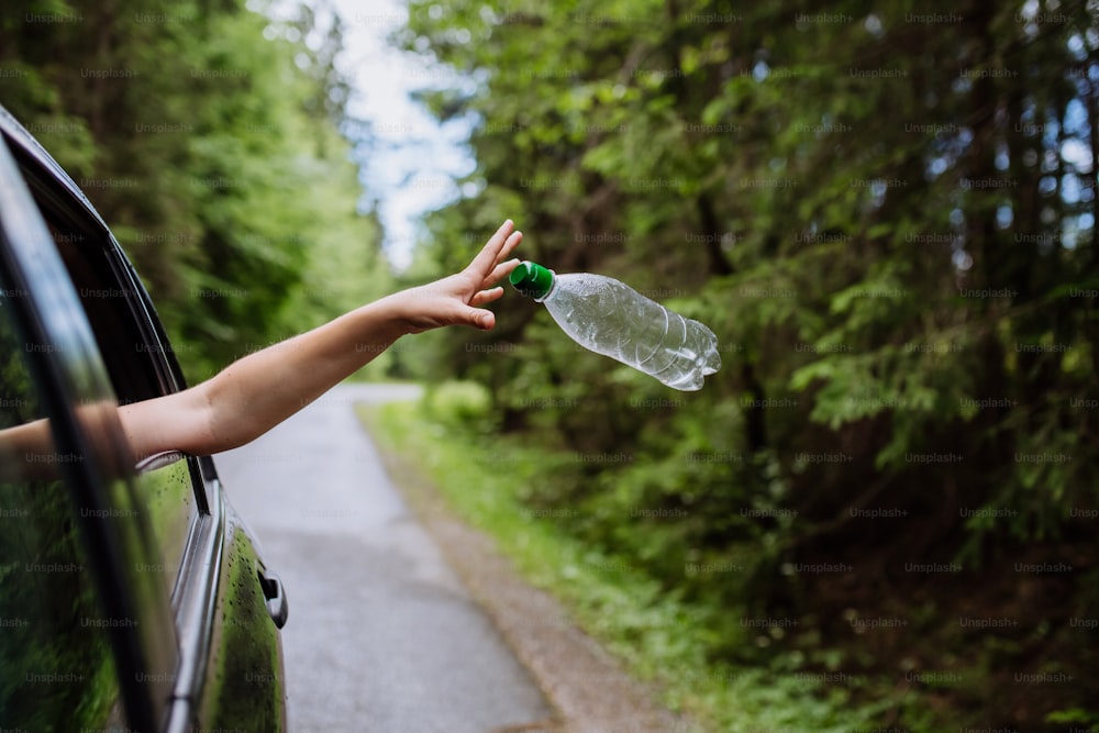 La mano de una mujer tirando la botella de plástico de la ventana del coche en la carretera en la naturaleza verde, protección del medio ambiente, concepto de calentamiento global