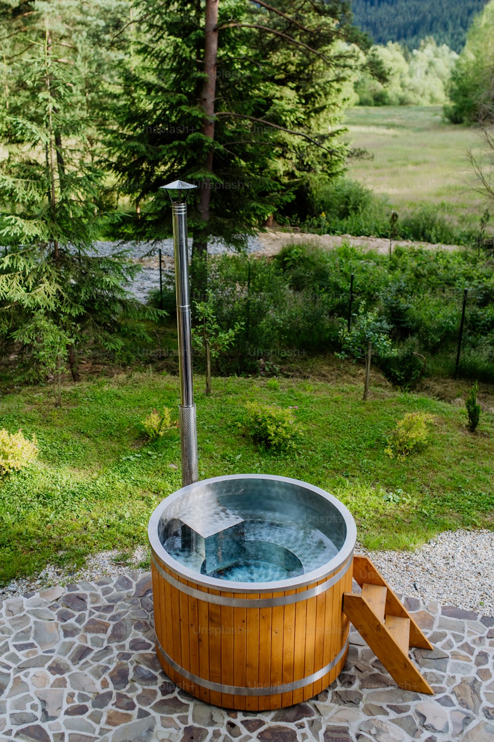 A wooden bathtub with a fireplace to burn wood and heat water in backyard in mountains.