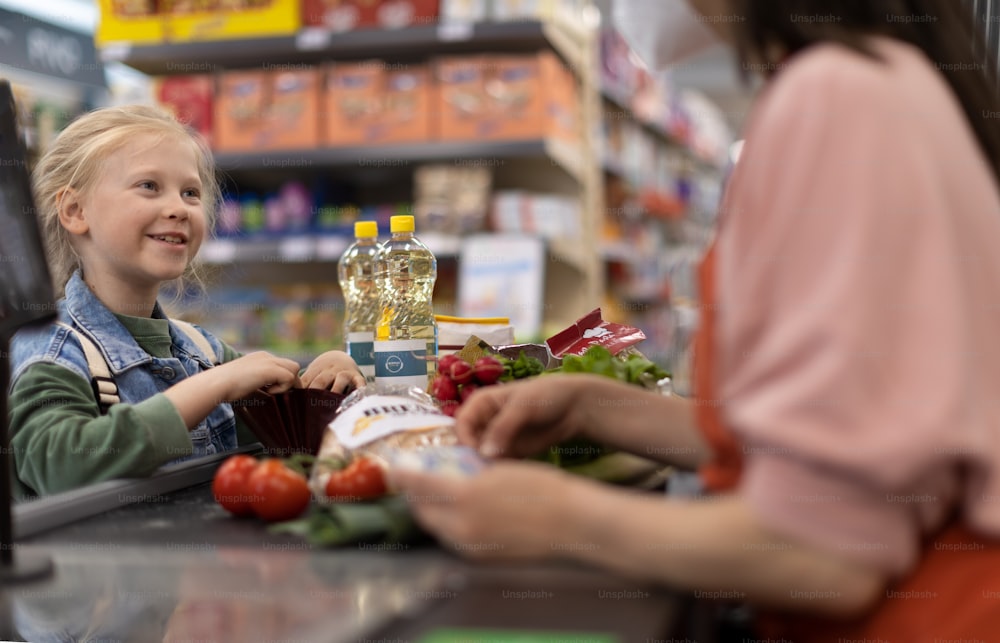 Gros plan d’une petite fille blonde qui paie ses courses au supermarché.
