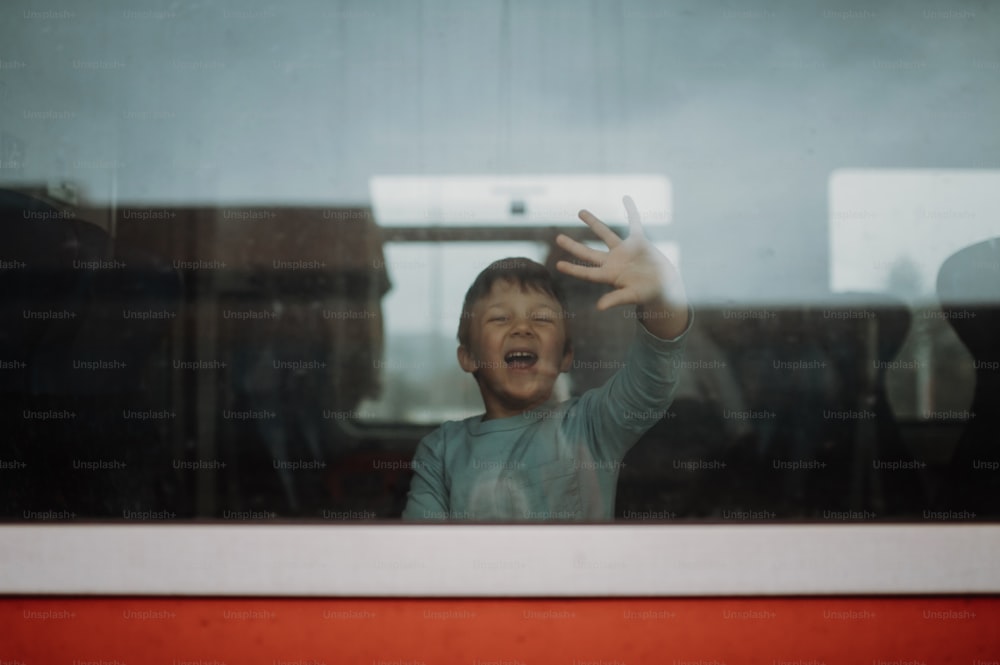 A happy little boy waving through window to say goodbye when travelling in train.