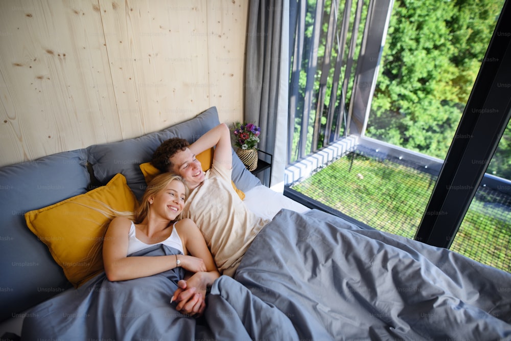 Una giovane coppia felice innamorata sdraiata a letto al mattino nella loro nuova casa in una piccola casa, concetto di vita sostenibile.