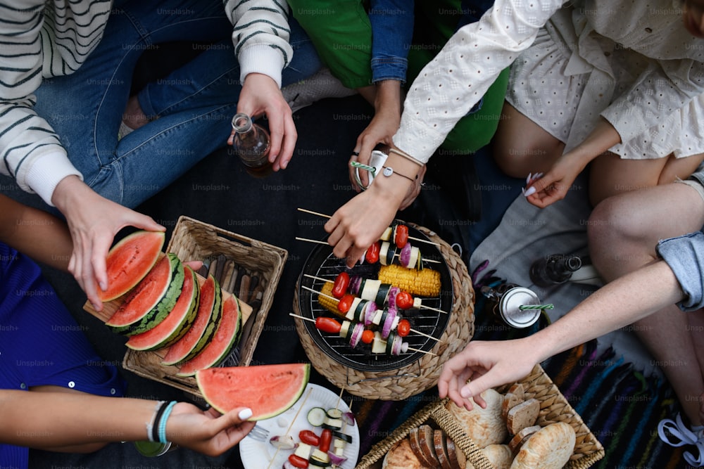 Nahaufnahme von jungen Freunden, die Mais und Spieße auf den Grill legen und grillen, wenn sie auf dem Campingplatz campen.