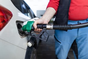 A senior worker standing on gas station and fueling car.