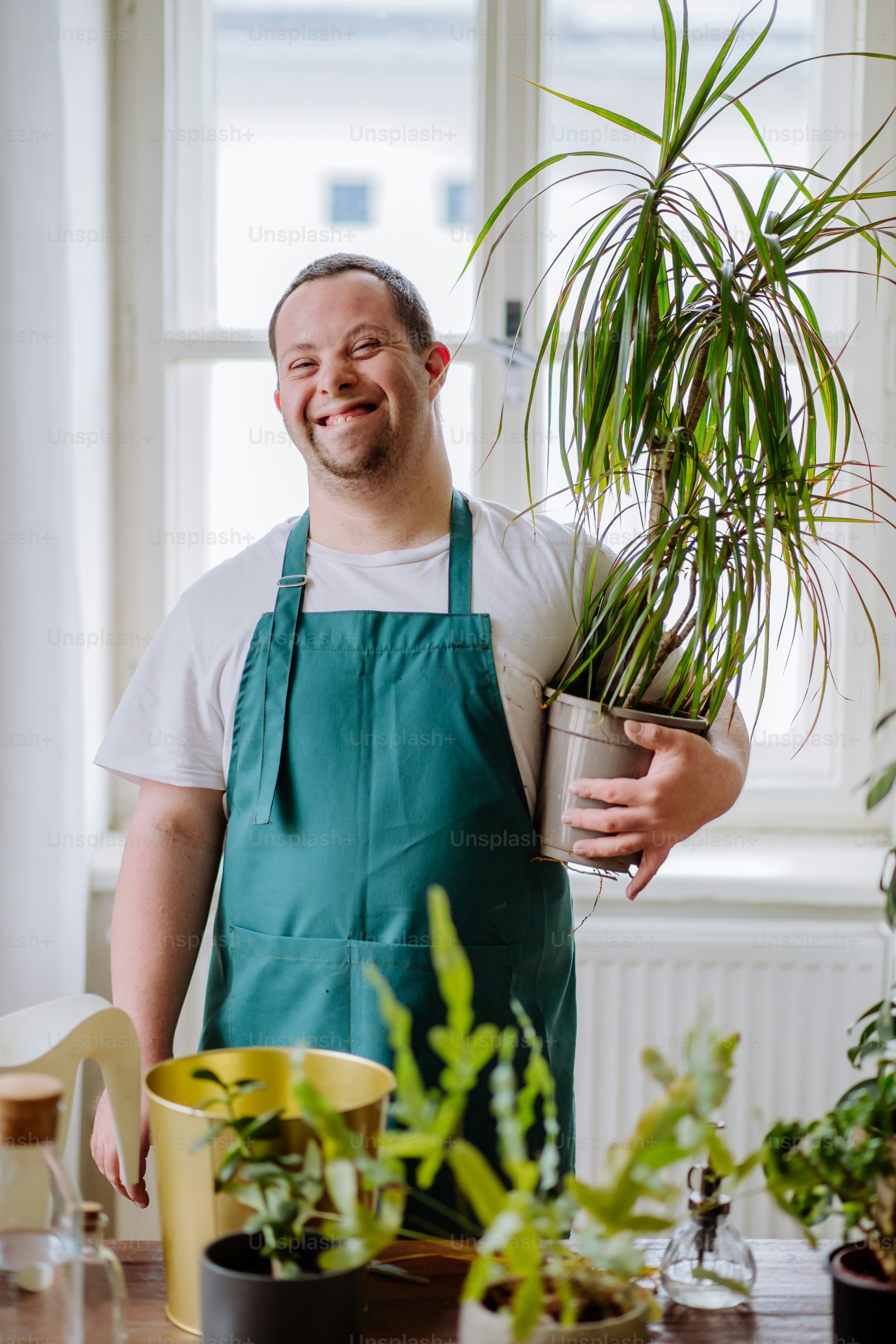 A young man with Down syndrome taking care of plants at home, smiling and looking at camera