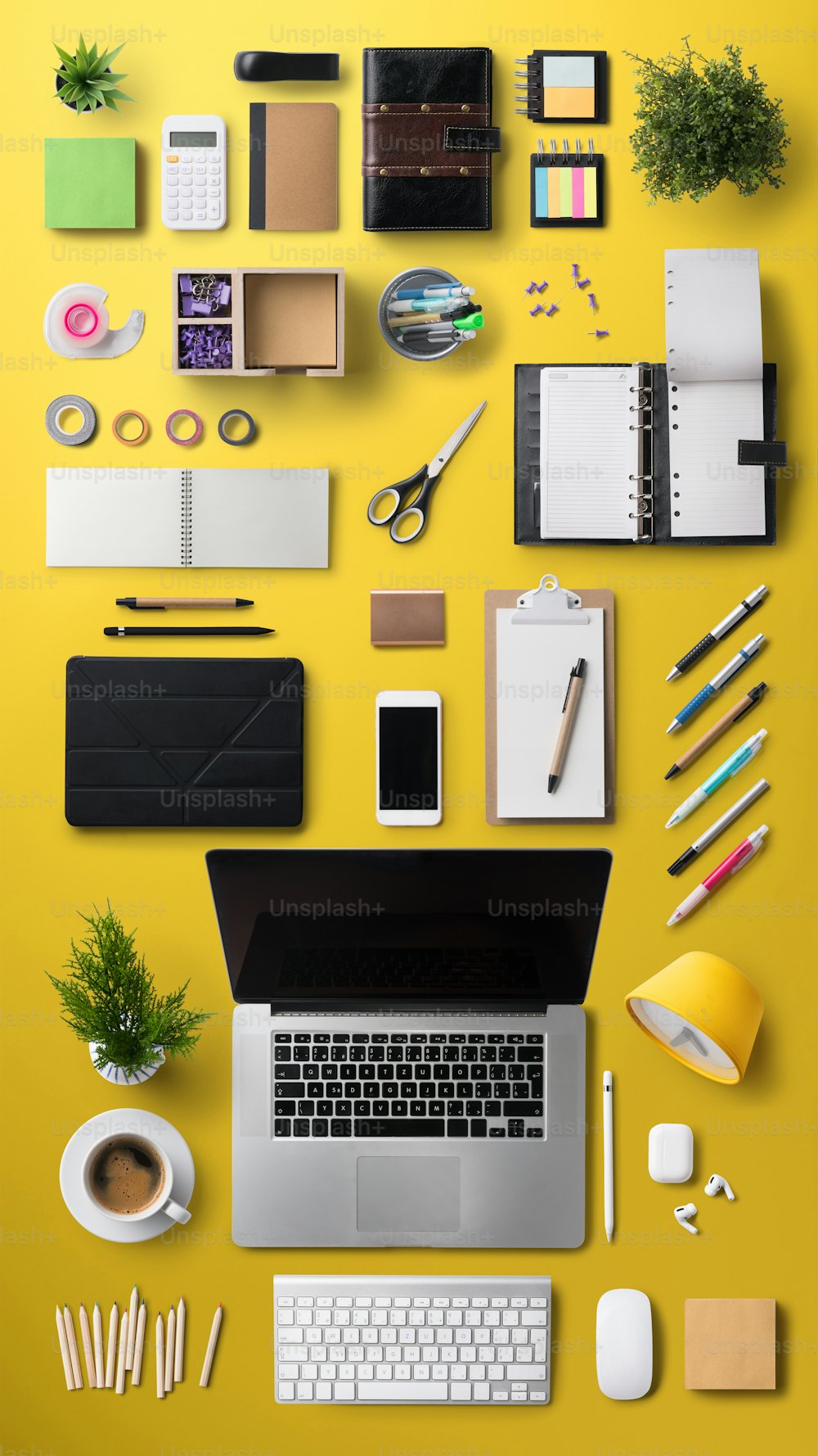 Spazio di lavoro della scrivania dell'ufficio con vista dall'alto con laptop, tablet, smartphone e forniture su sfondo giallo.