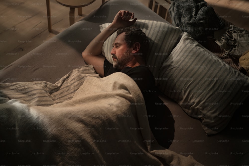 코로나 우울증을 앓고 있는 슬픈 성숙한 남자가 밤에 침대에 누워 있다.