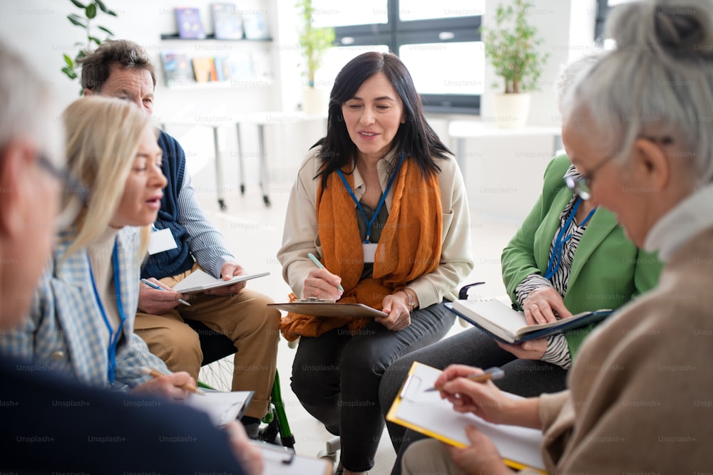 Aufgeregte ältere Menschen, die an einer Gruppentherapiesitzung im Pflegeheim teilnehmen, positive ältere Männer und Frauen sitzen im Kreis und unterhalten sich mit dem Psychologen