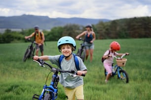 A portrait of young family with little children preapring for bike ride, standing with bicycles in nature.