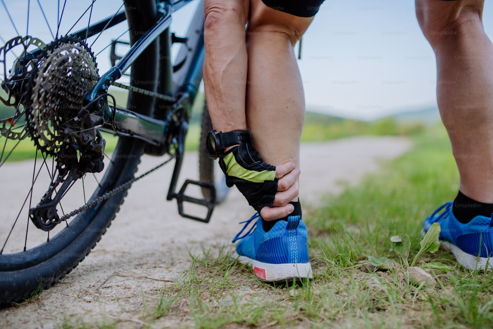 Um close-up de um homem idoso ativo em roupas esportivas sufocando de dor no tornozelo depois de andar de bicicleta, no parque no verão.