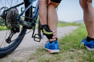 Un primo piano di un uomo anziano attivo in abbigliamento sportivo che soffoca dal dolore alla caviglia dopo aver pedalato, nel parco in estate.