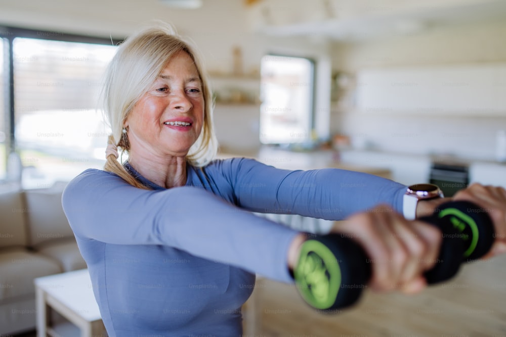 A fit senior woman exercising with dumbbells at home, active lifestyle concept.