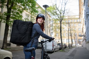 Uma mensageiro feminina em bicicleta com mochila térmica a caminho de entregar comida aos clientes.