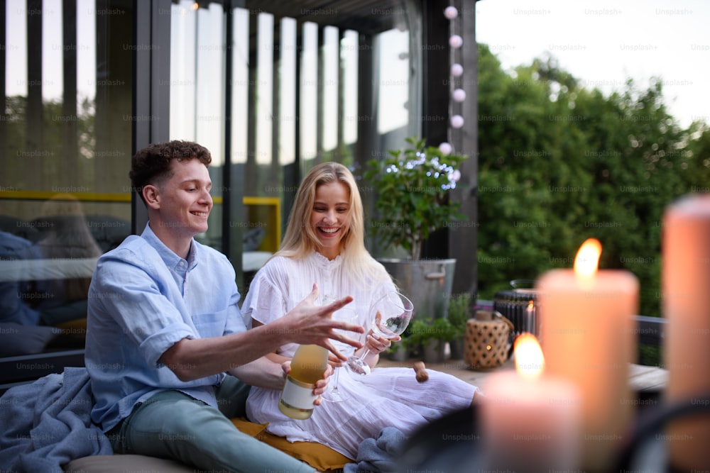 Ein junges Paar, das eine Flasche Champagner im Freien öffnet und feiert, Wochenende in einem kleinen Haus auf dem Land, nachhaltiges Leben.