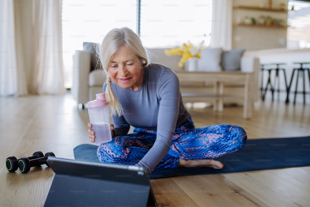 Eine fitte ältere Frau, die zu Hause Stretching-Übungen mit Tutorial auf dem Tablet macht, aktives Lebensstilkonzept.