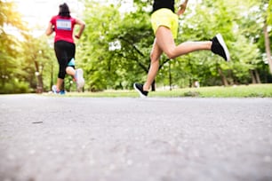 Close up of legs of young athletes running in green sunny summer park.