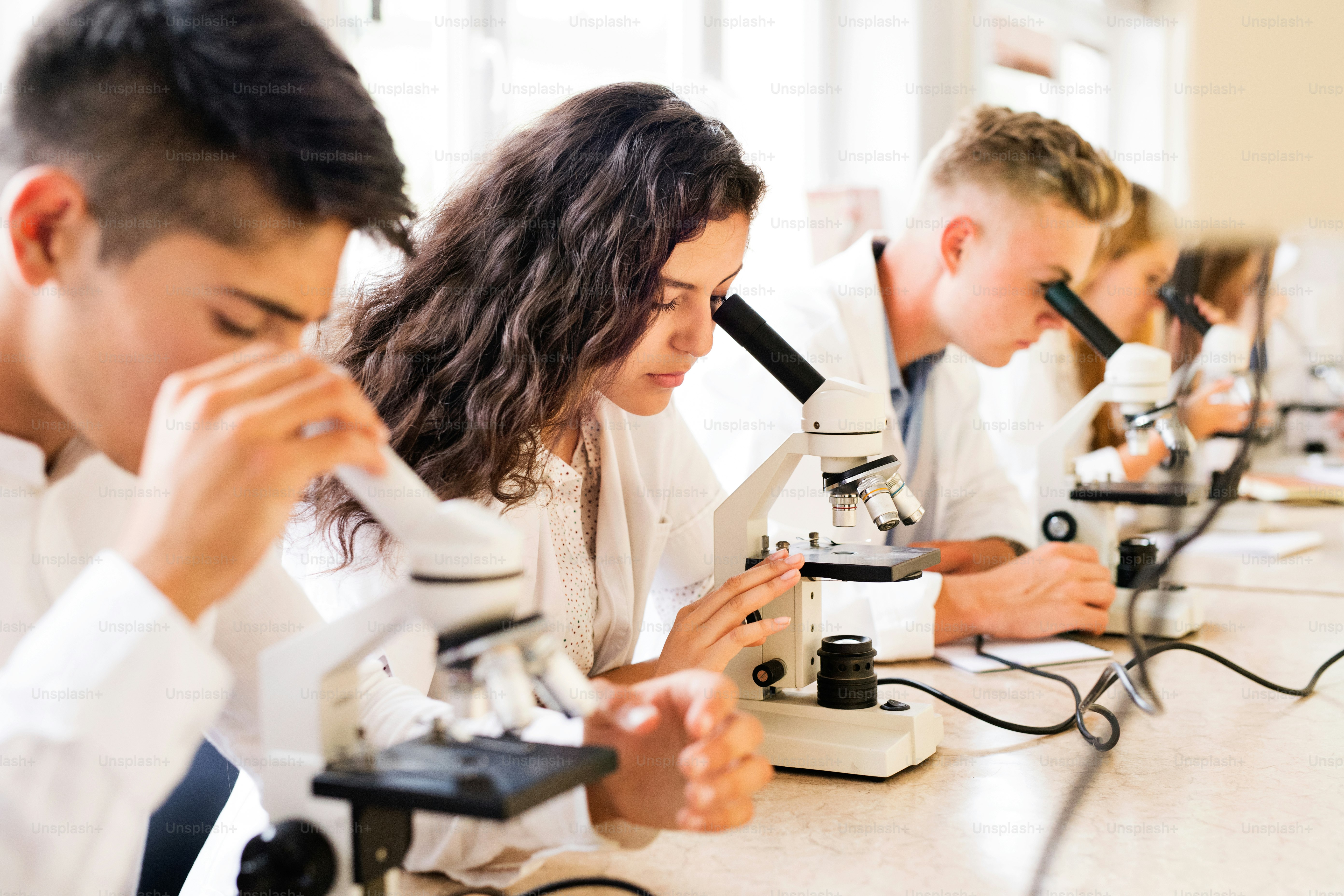 Beautiful high school students with microscopes in laboratory during ...