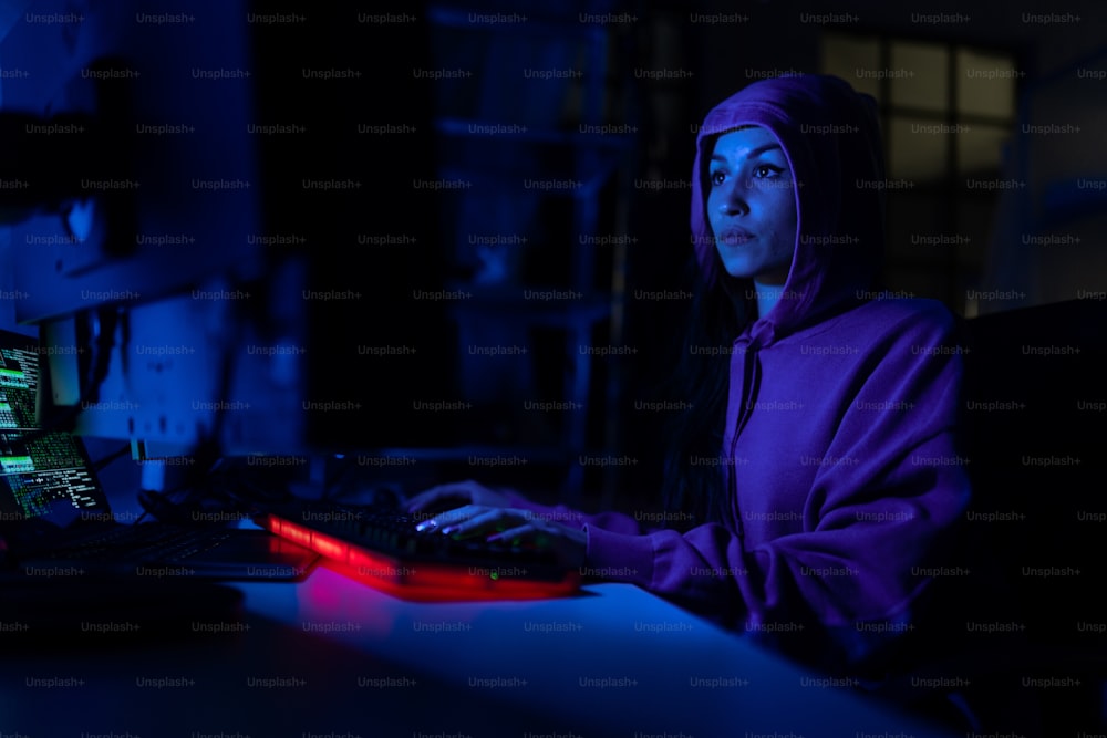 A young woman hacker by computer in the dark room at night, cyberwar concept.
