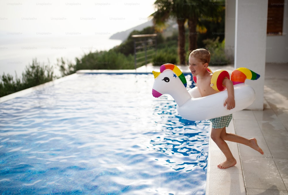 Un bambino felice che si diverte quando salta in piscina con unicorno ad anello gonfiabile. Attività acquatica estiva all'aperto per bambini.
