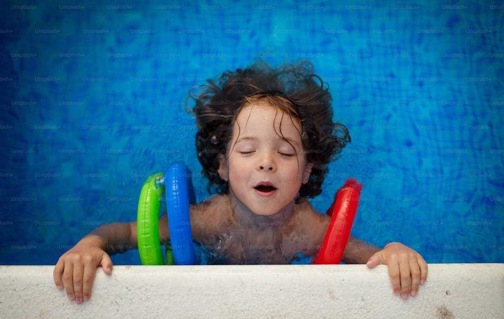 Una vista dall'alto di un bambino felice che indossa bracciali gonfiabili che impara a nuotare in piscina. Concetto di vacanza estiva.