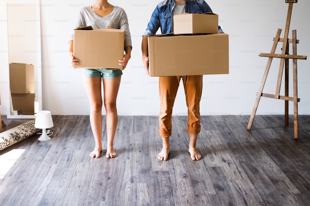 Jovem casal irreconhecível que se muda para uma nova casa, segurando grandes caixas de papelão.