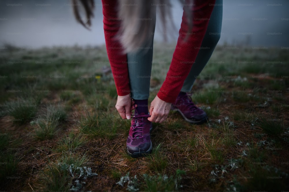 Un primer plano de una mujer mayor atándose los cordones de los zapatos antes de hacer ejercicio en la naturaleza temprano en la mañana con niebla.