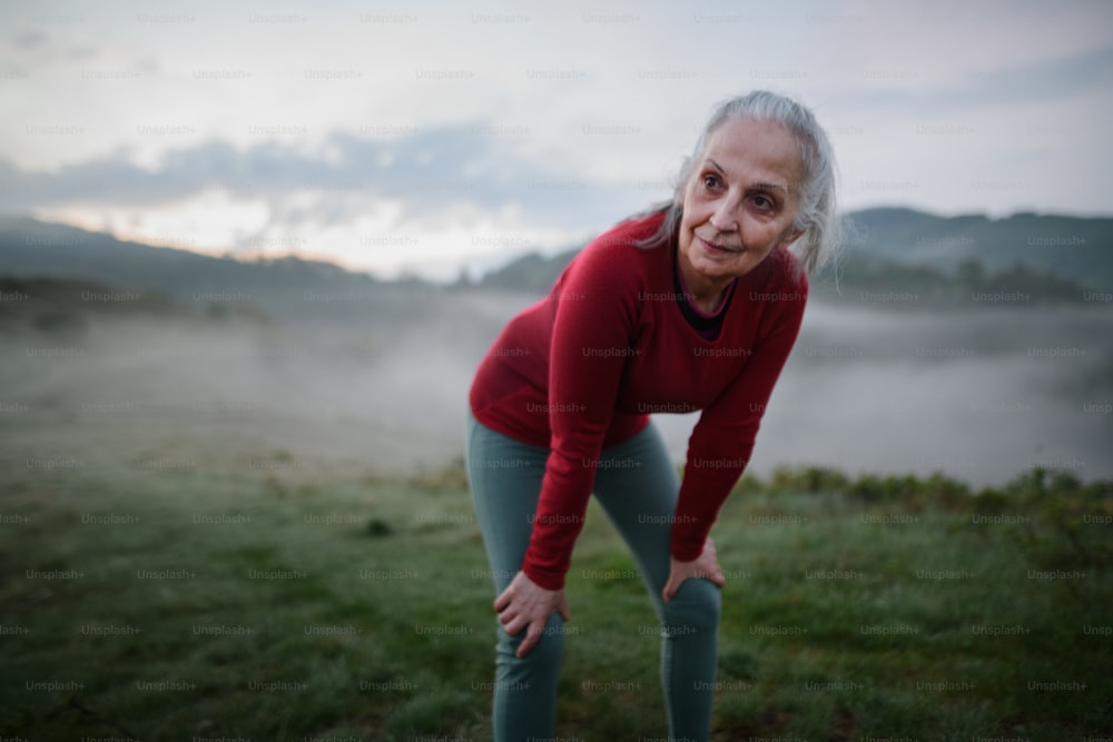 Une femme âgée faisant des exercices de respiration dans la nature tôt le matin avec du brouillard et des montagnes en arrière-plan.