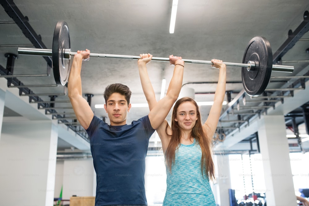 Beautiful young fit couple exercising in modern gym, lifting heavy barbell.