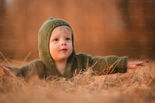 An autumn portrait of happy little boy in knitted sweater lying on front in dry grass in nature and having fun.