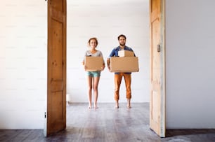 Young married couple moving in new house, holding big cardboard boxes.