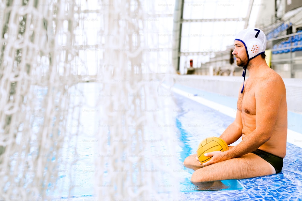 Water polo player sitting on the edge of a swimming pool. Man doing sport.