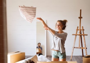 Young married couple moving in a new house, woman unpacking things from a cardboard box.