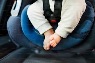 Legs of unrecognizable little baby girl fastened with security belt in safety car seat.