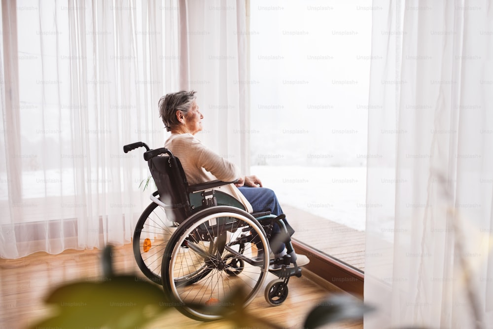Mujer mayor en silla de ruedas en casa mirando por la ventana.
