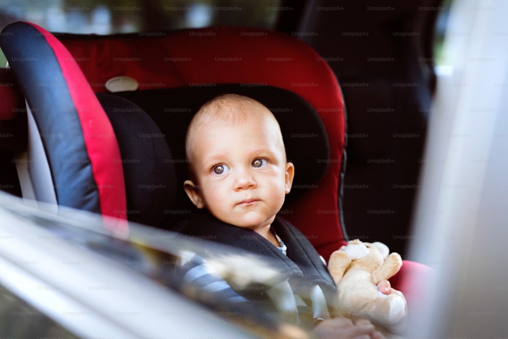 Bambino carino seduto nel seggiolino dell'auto in macchina, guardando fuori. Primo piano.