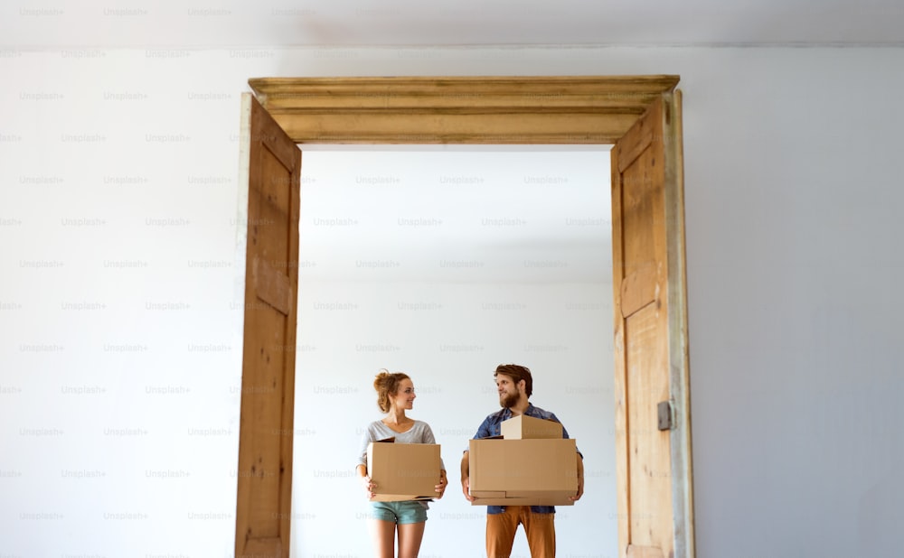 Young married couple moving in new house, holding big cardboard boxes.