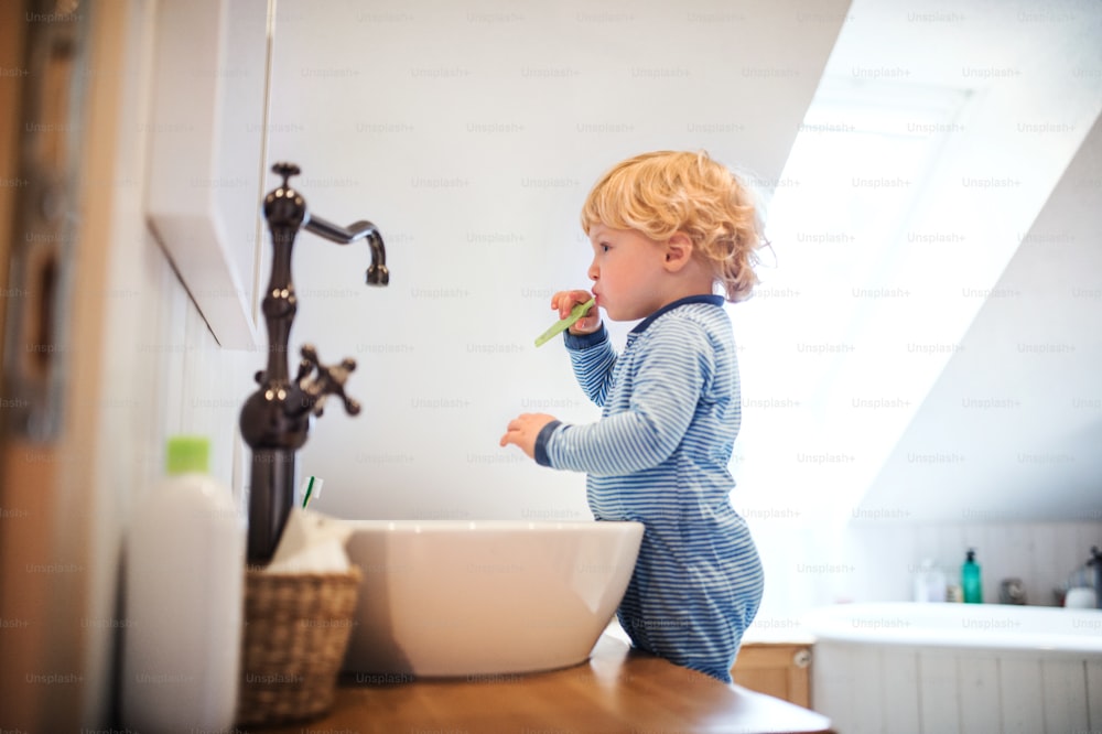 Süßes Kleinkind, das sich im Badezimmer die Zähne putzt. Kleiner Junge, der auf einem Hocker vor dem Spiegel steht.