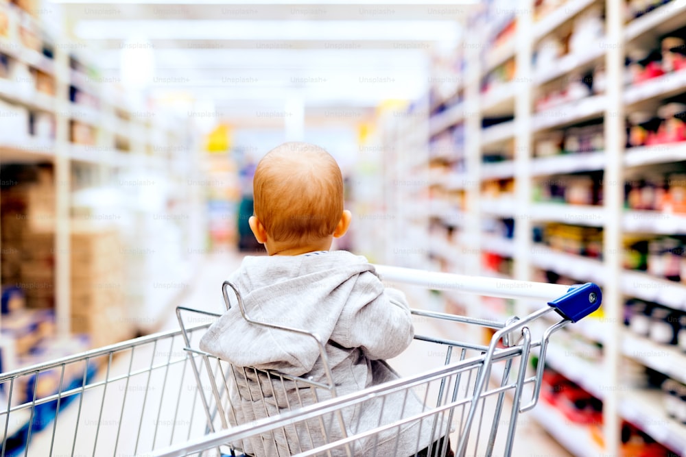 슈퍼마켓에서 귀여운 작은 아기. 쇼핑 트롤리에 앉아 있는 아기. 후면도.