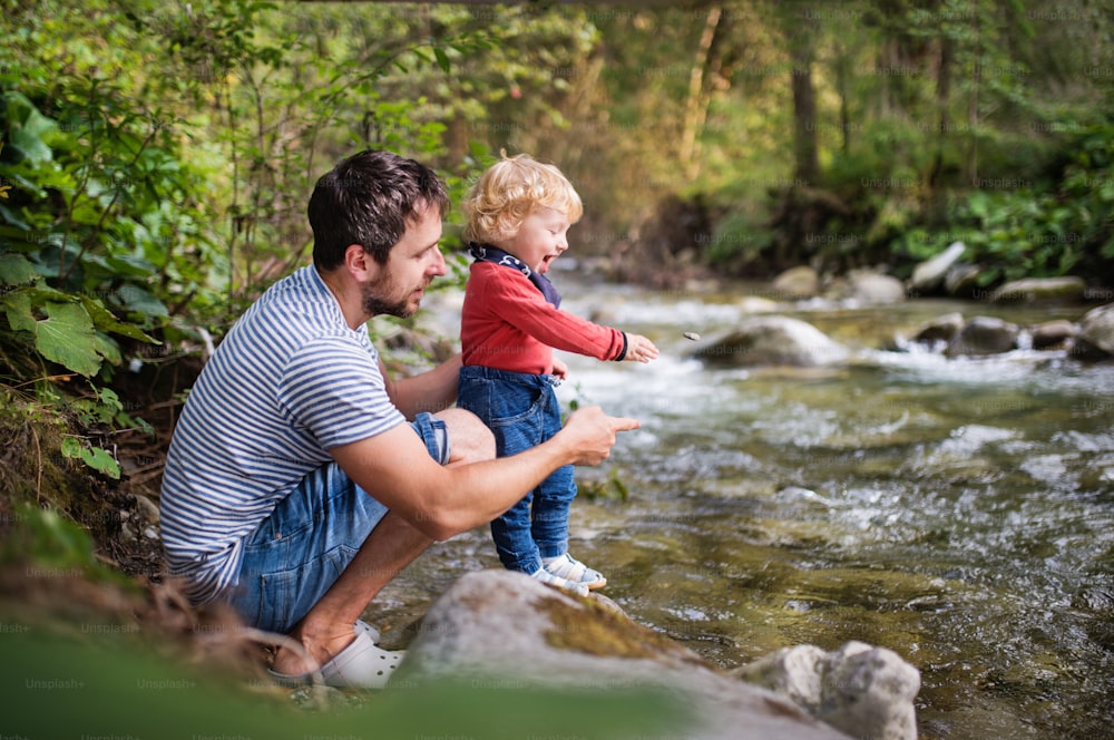 Pai jovem com menino feliz no rio, dia de verão.