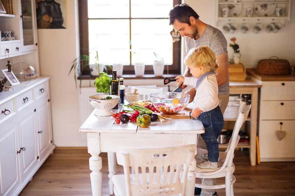 よちよち歩きの男の子と料理をする若い父親。野菜サラダを作る息子と男性。