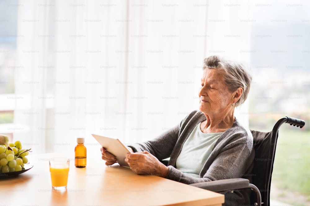 Senior woman in a wheelchair with tablet at home. An elderly woman sitting at the table.