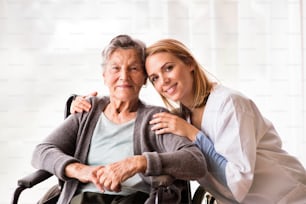 Visitatore sanitario e una donna anziana durante la visita domiciliare. Ritratto di un'infermiera e di una donna anziana su una sedia a rotelle.