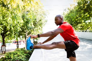 Junger afroamerikanischer Läufer in der Stadt, der sich aufwärmt und seine Beine ausstreckt.