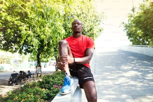 Joven corredor afroamericano en la ciudad sentado en el muro de hormigón, descansando.